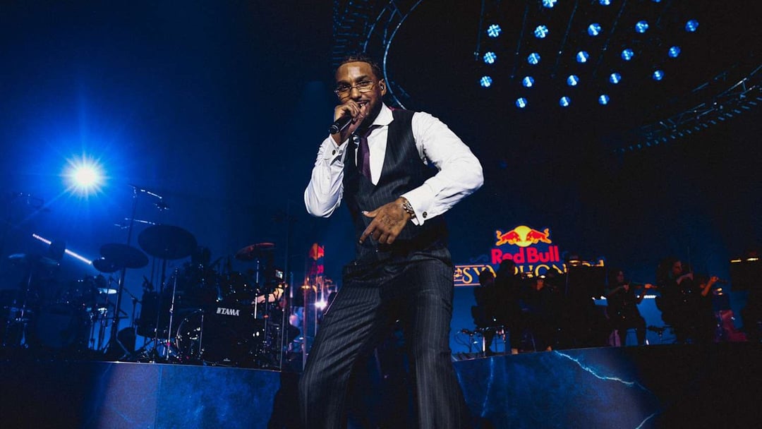 A male singer in a vest and pinstriped suit performs on a dark stage, holding a microphone. Blue stage lights illuminate the performer and musical instruments in the background. REDBULL SYMPHONIC by Chris Schwarz for RedBull — © EASYdoesit.