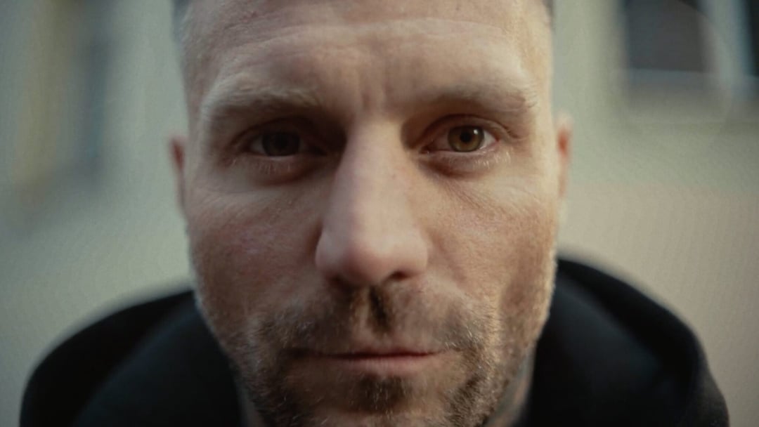 Close-up of a man's face with short hair and stubble, looking directly at the camera. KONTRA K – TRAILER by Christoph Szulecki for Kontra K — © EASYdoesit.